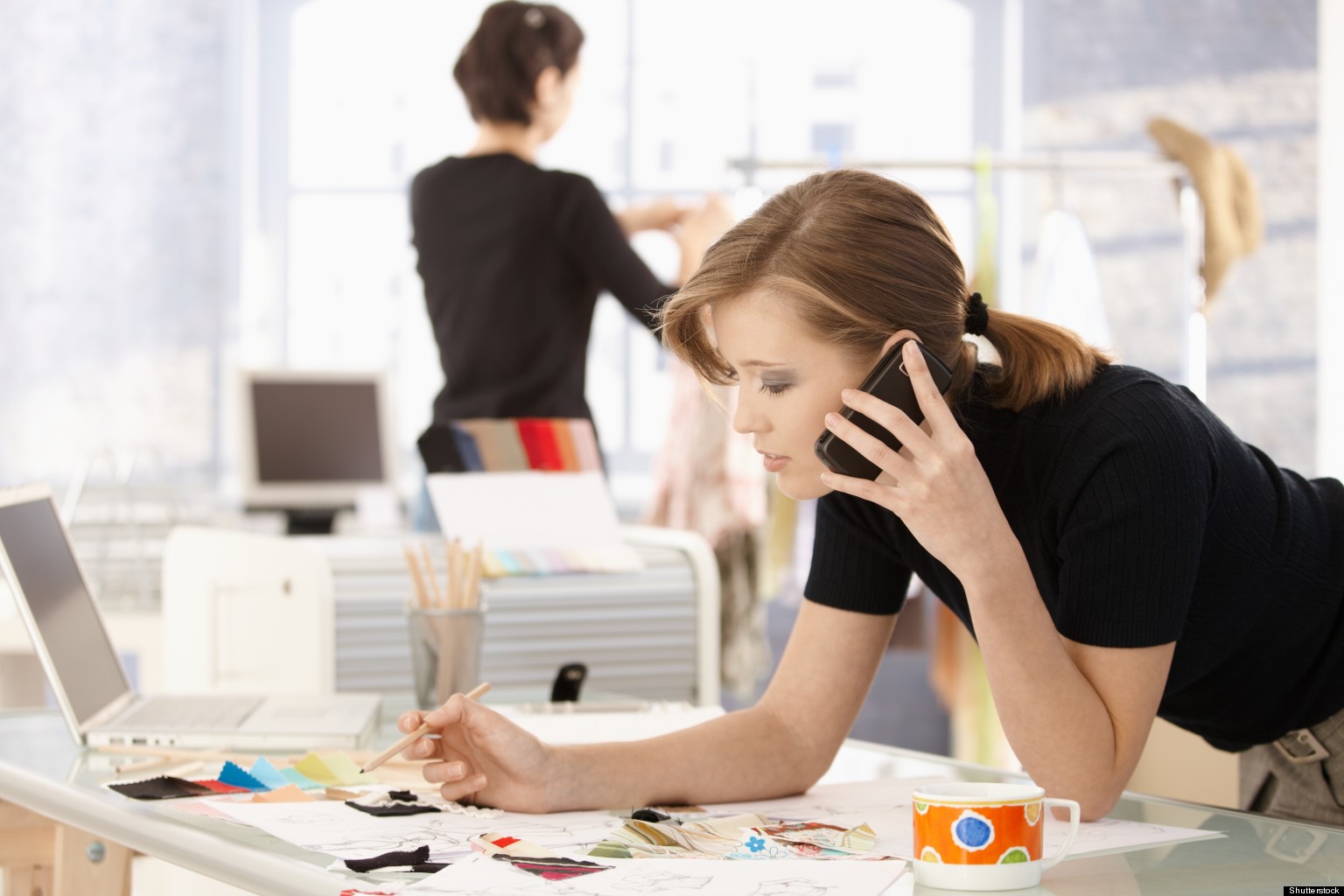 Young attractive female fashion designer leaning on office desk, talking on mobile phone.?; Shutterstock ID 78531826; PO: The Huffington Post; Job: The Huffington Post; Client: The Huffington Post; Other: The Huffington Post