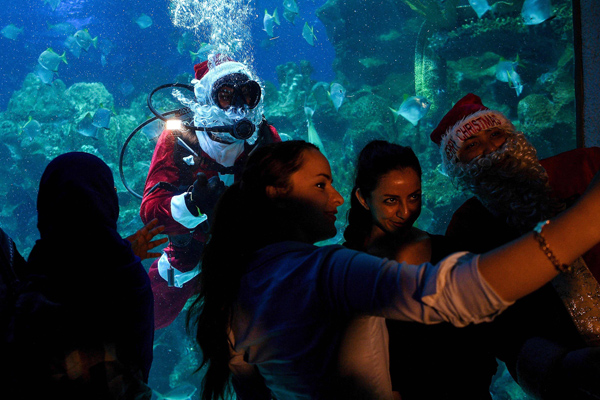 Visitors pose for a selfie with a diver dressed as Santa Claus inside a fish-tank at the Aquaria KLCC in Kuala Lumpur on December 8, 2016. The scuba-diving Santa Claus is one of the prime attractions in conjunction with Christmas festivities for visitors at the underwater park. / AFP / Manan VATSYAYANA